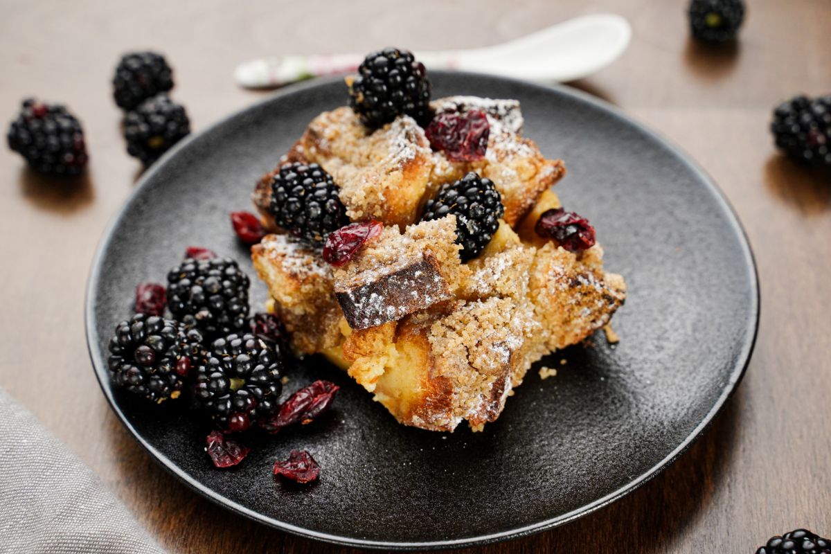 black plate of berries and french toast with white spoon in background
