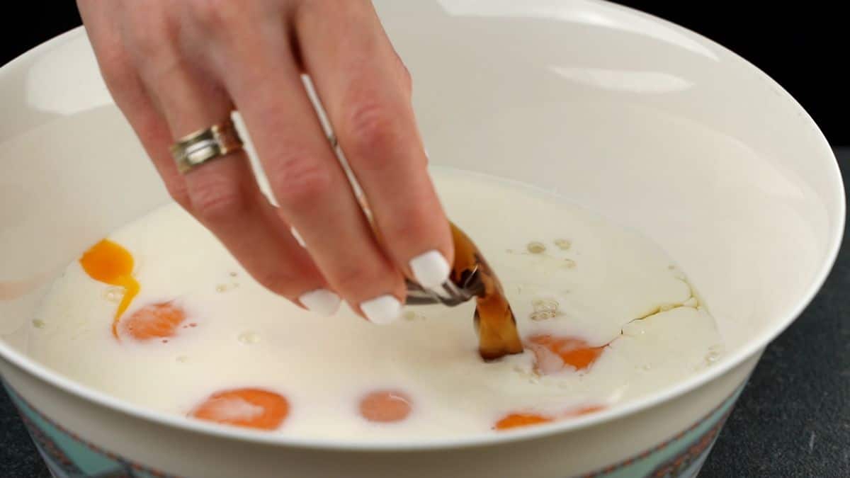 vanilla being poured into milk and eggs in white bowl