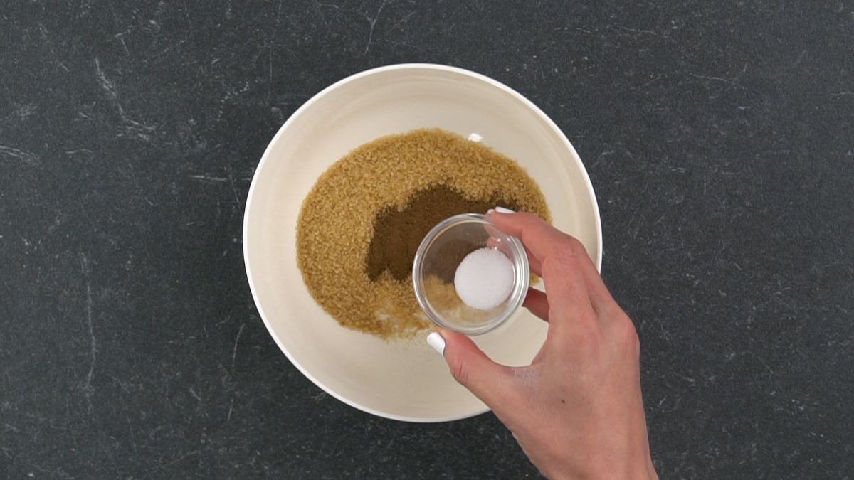 sugar being poured over brown sugar in white bowl