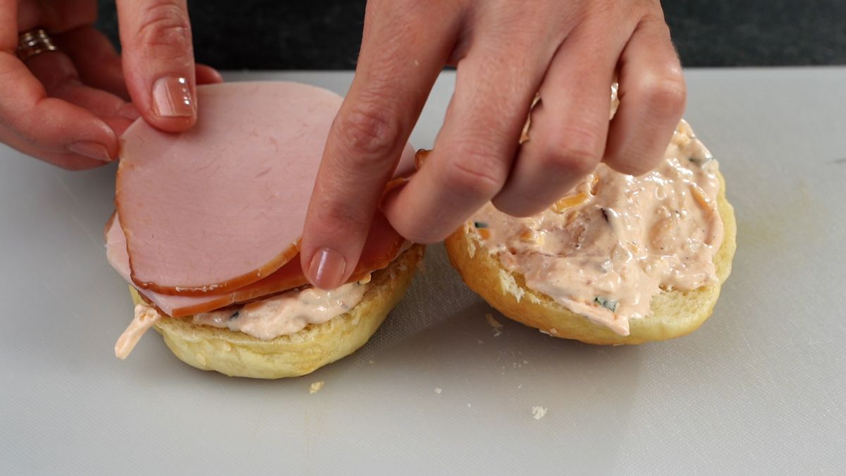 sliced ham being placed on top of cheesy bun