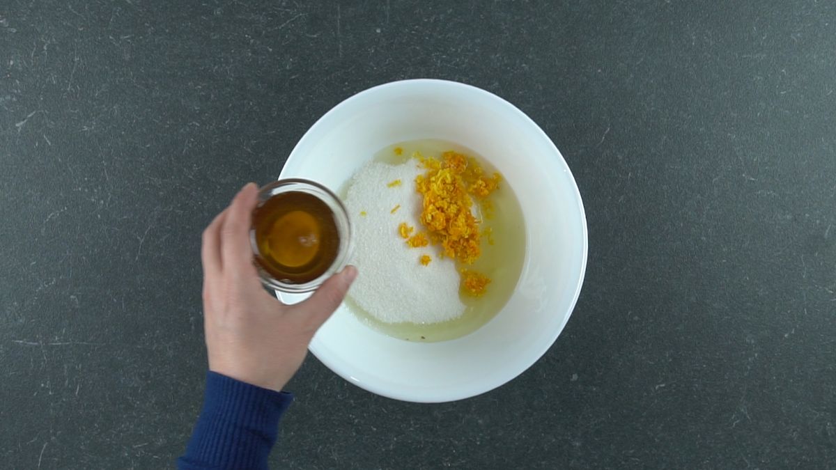 honey in small glass bowl being held above white bowl of sugar and egg