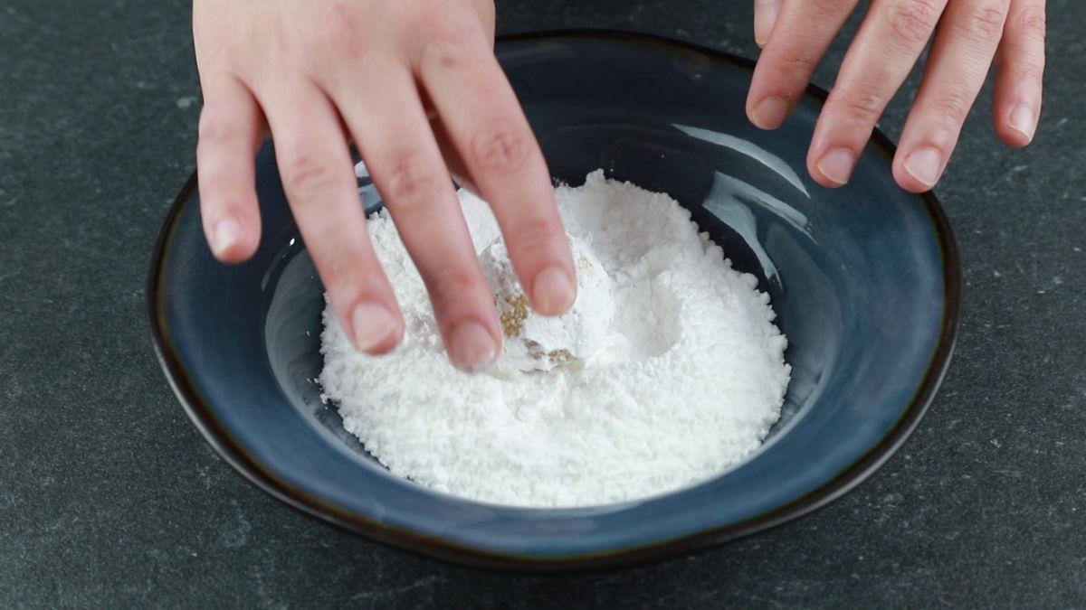 hand rolling dough ball in powdered sugar