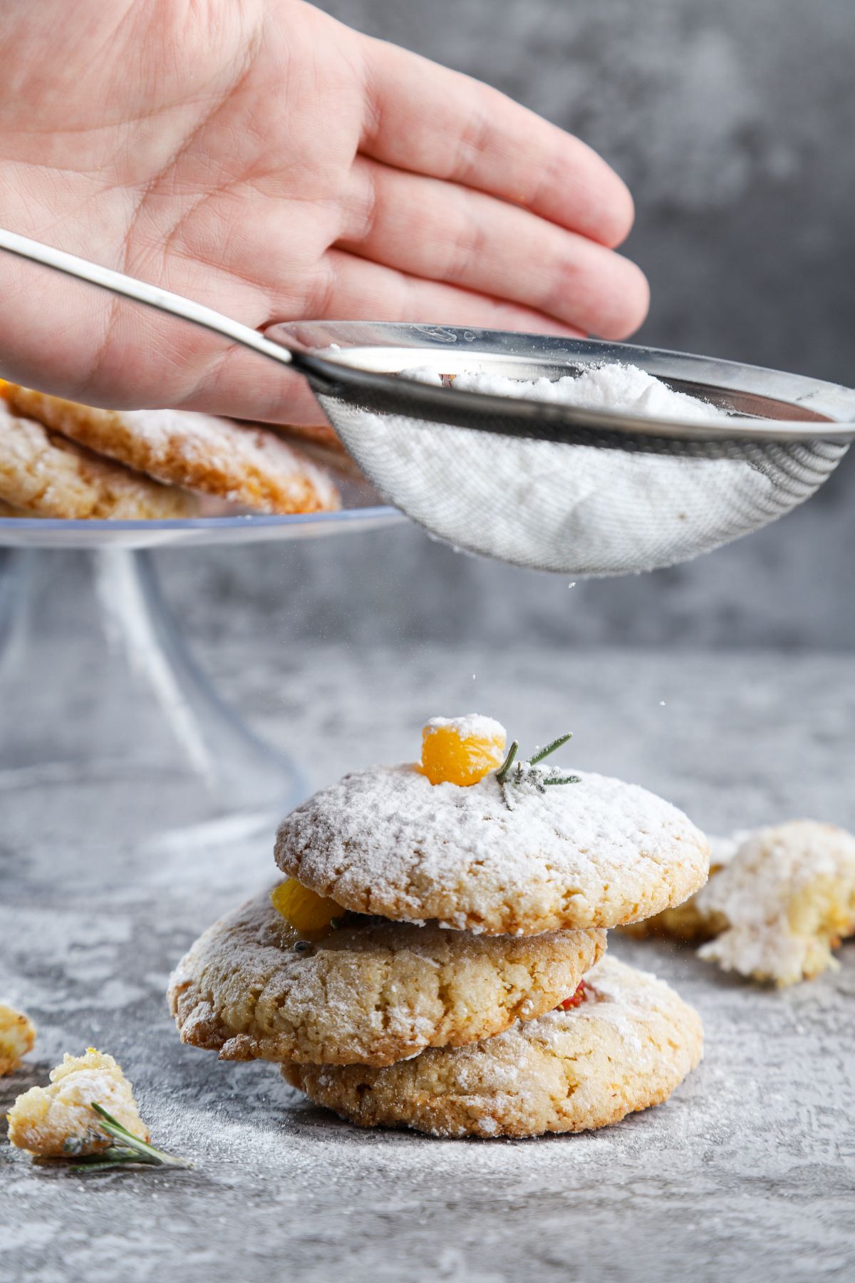 hand tapping sieve of powdered sugar over stack of cookies