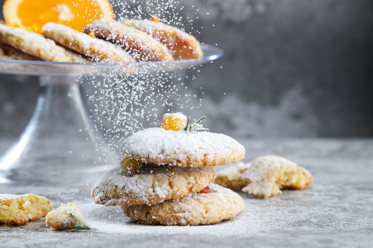 orange cookies on grey table with powdered sugar being sprinkled on them