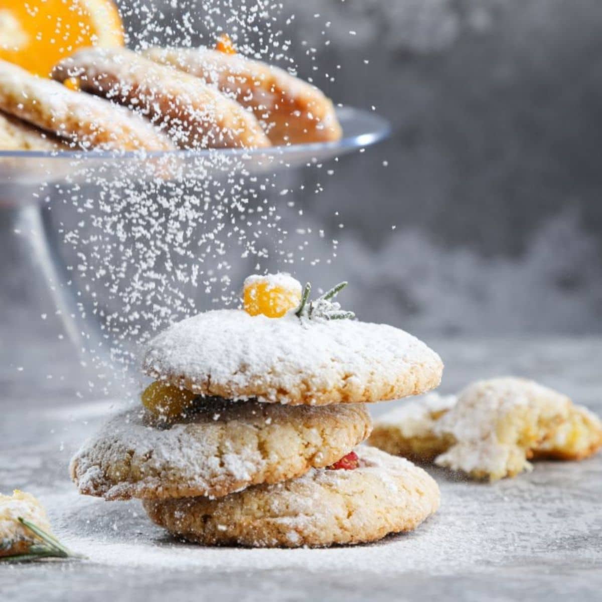 orange cookies on grey table with powdered sugar being sprinkled on them