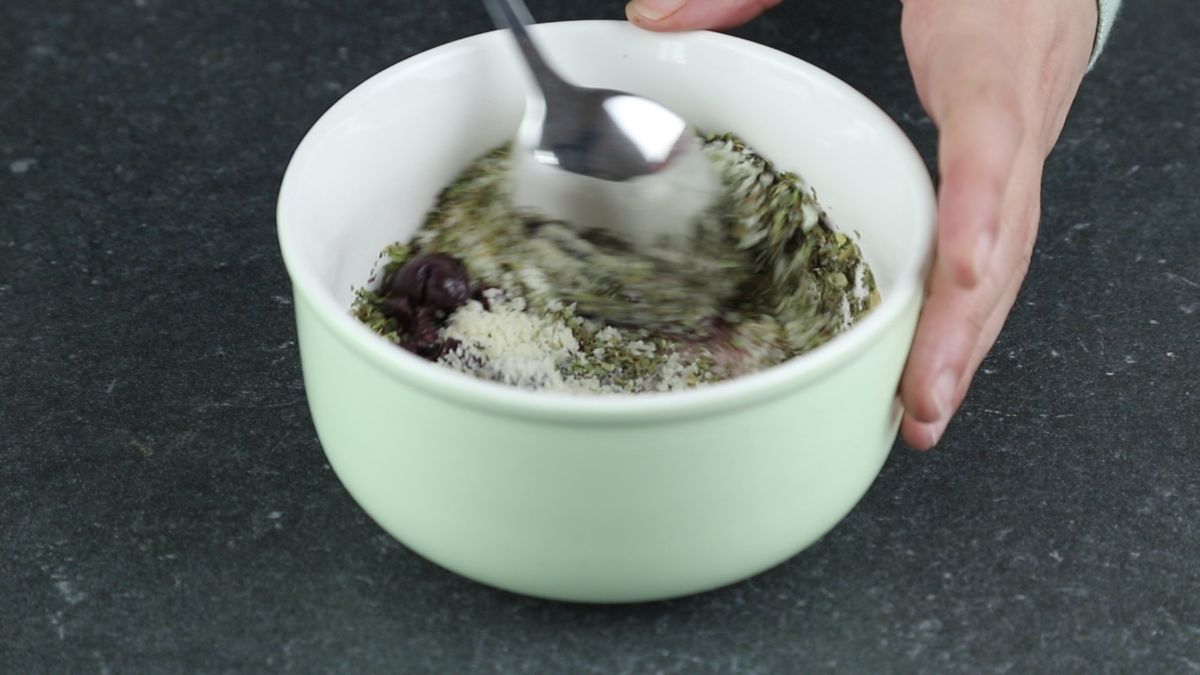 spoon in white bowl stirring salad dressing herbs