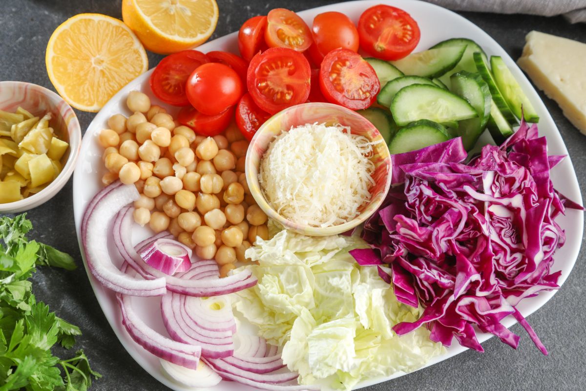 ingredients for salad on white platter with bowl of parmesan in middle