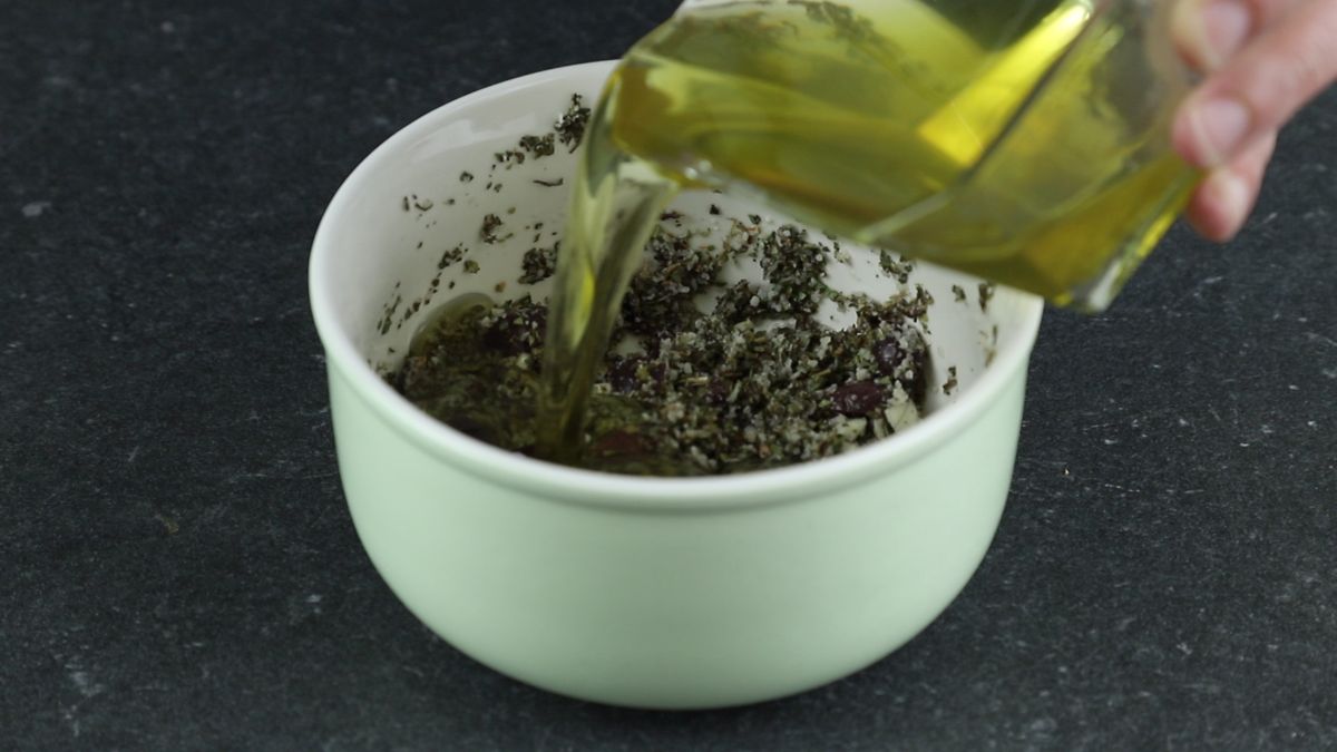 olive oil being poured into white bowl of herbs