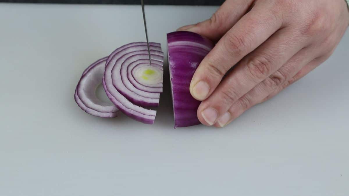 hand holding red onion and knife on cutting board