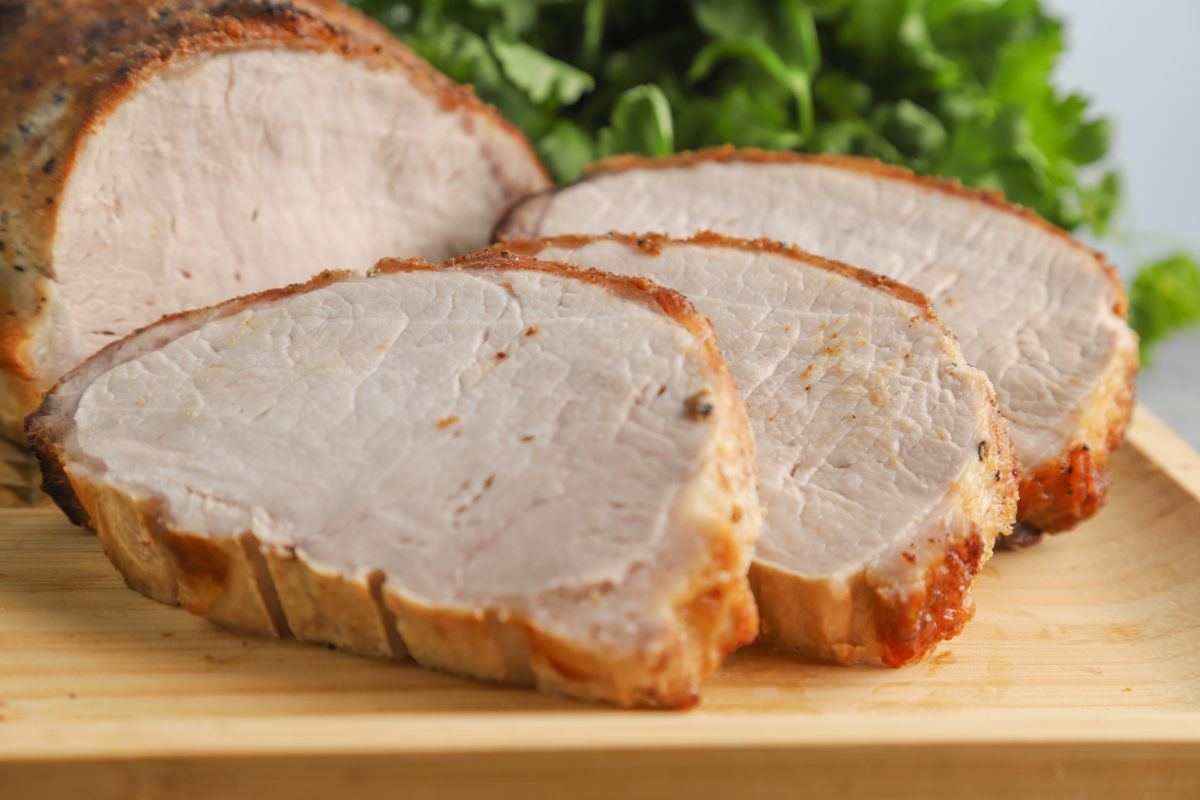 slices of pork loin on cutting board by fresh herbs