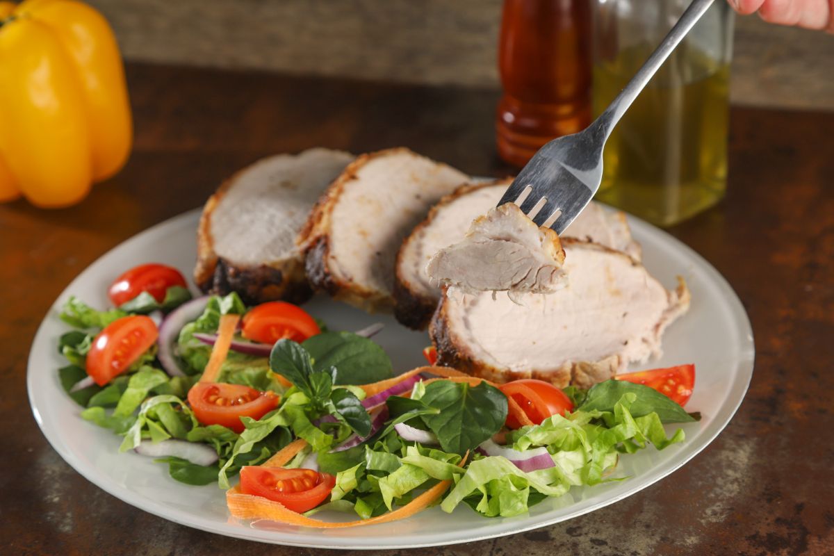 fork holding slice of pork loin above plate with salad greens and pork slices
