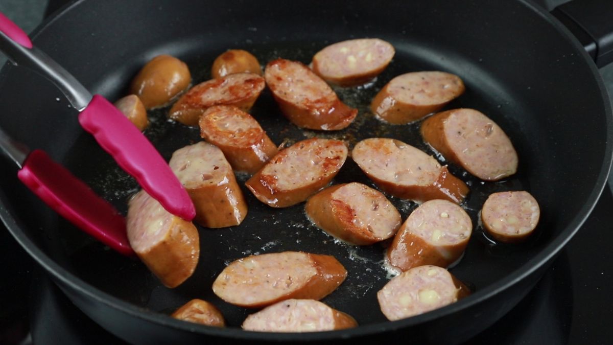 black skillet of sausages being turned with pink tongs