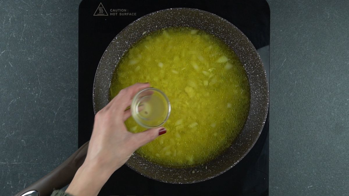 hand holding glass bowl of lemon juice above skillet of rice