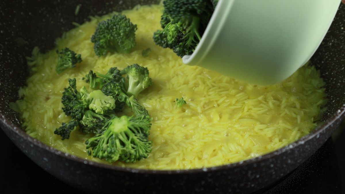 white bowl of broccoli hovering over black skillet of rice
