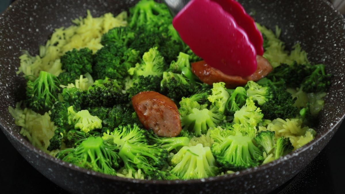 red tongs in skillet with broccoli and sausage
