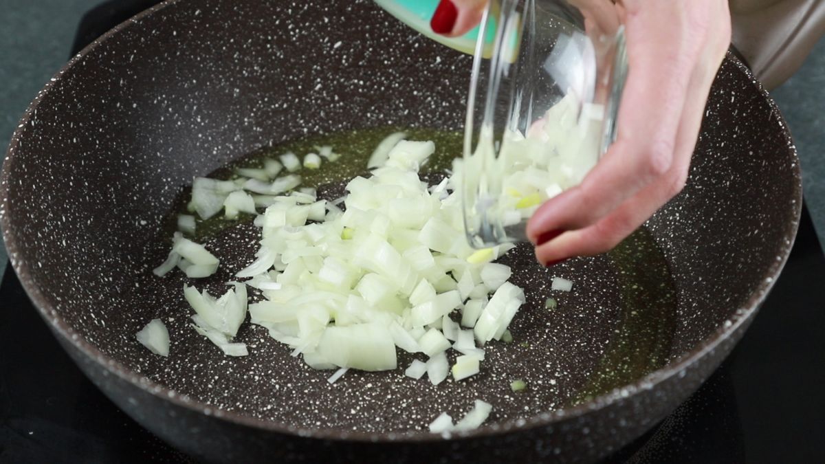 glass bowl of onions being poured into skillet