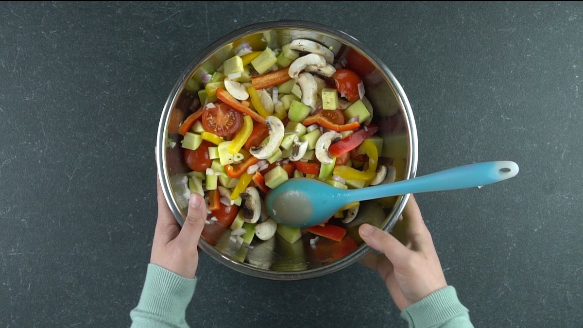 stainless steel bowl of vegetables with blue spoon in them