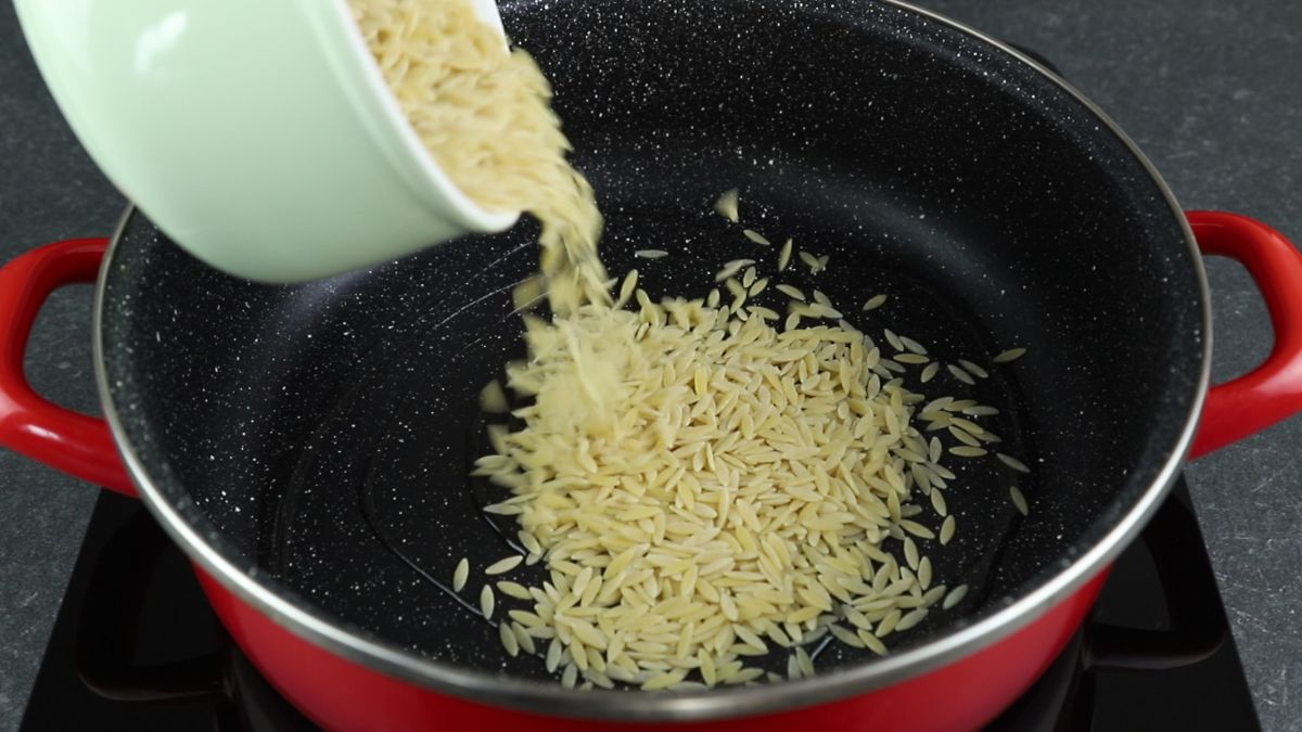 orzo pasta being poured into black and red stockpot