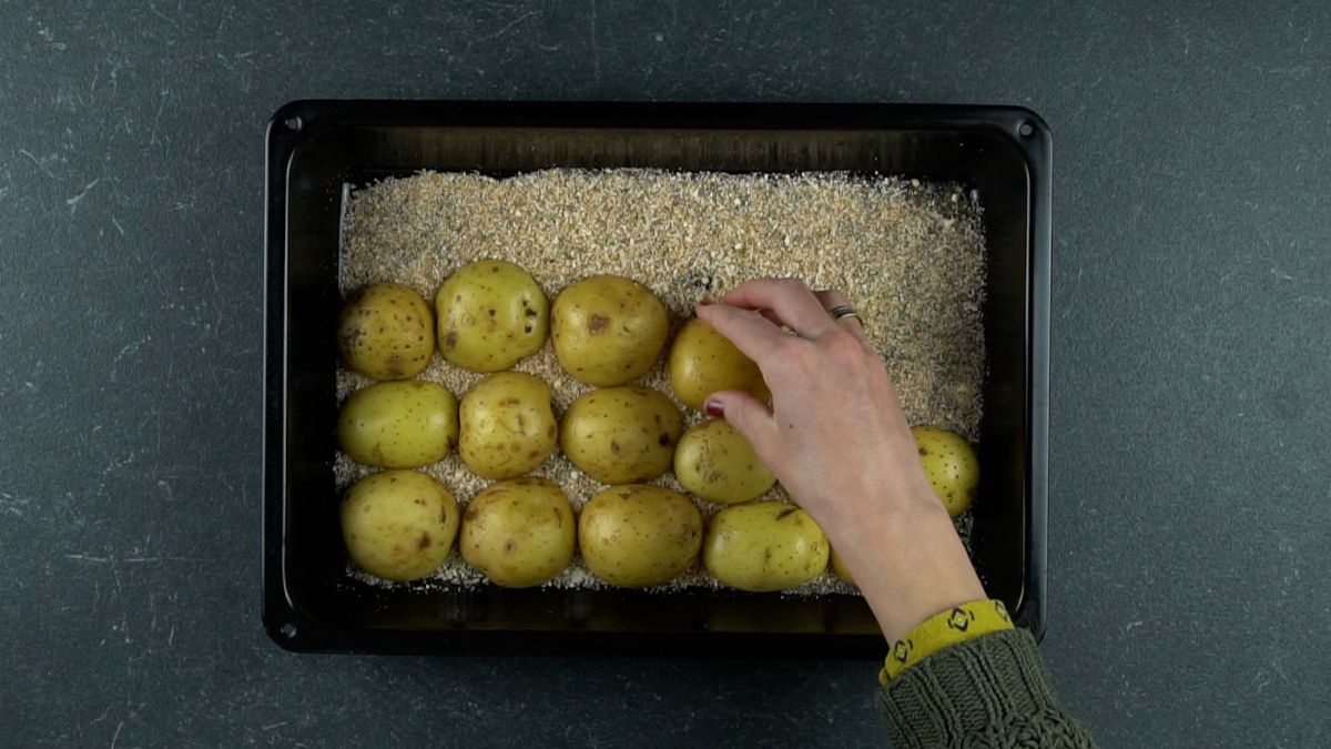 hand putting potato halves into pan of herbs and cheese