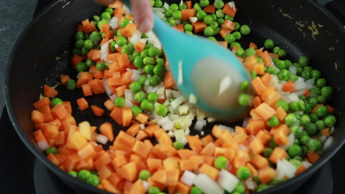 carrots, peas and onions in skillet with blue spoon