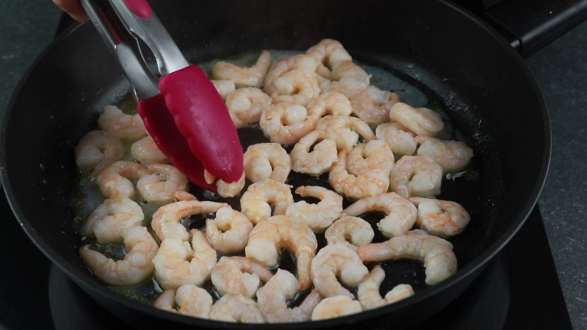 shrimp in skillet with pink tongs