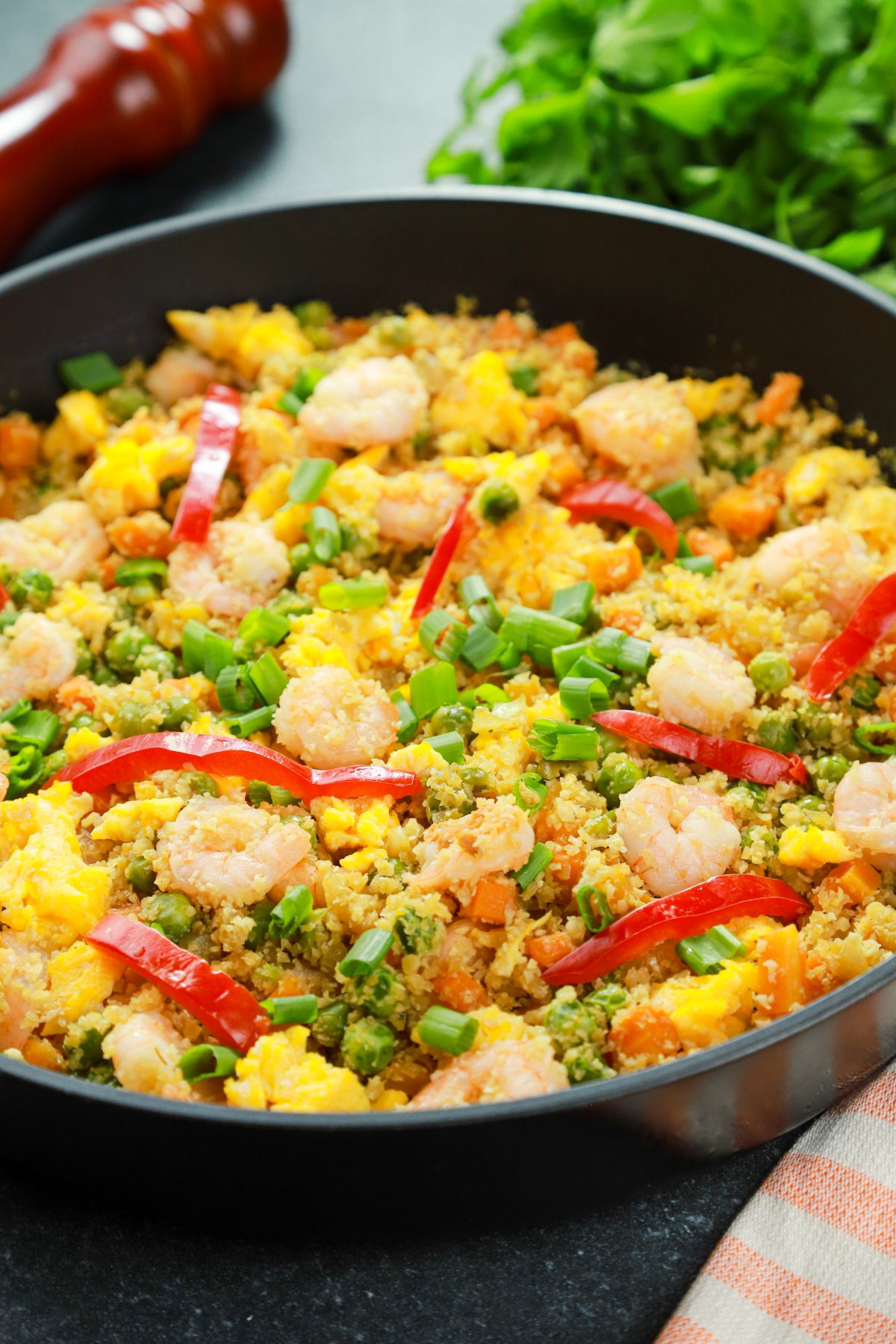 black skillet filled with cauliflower fried rice topped with shrimp and red bell pepper