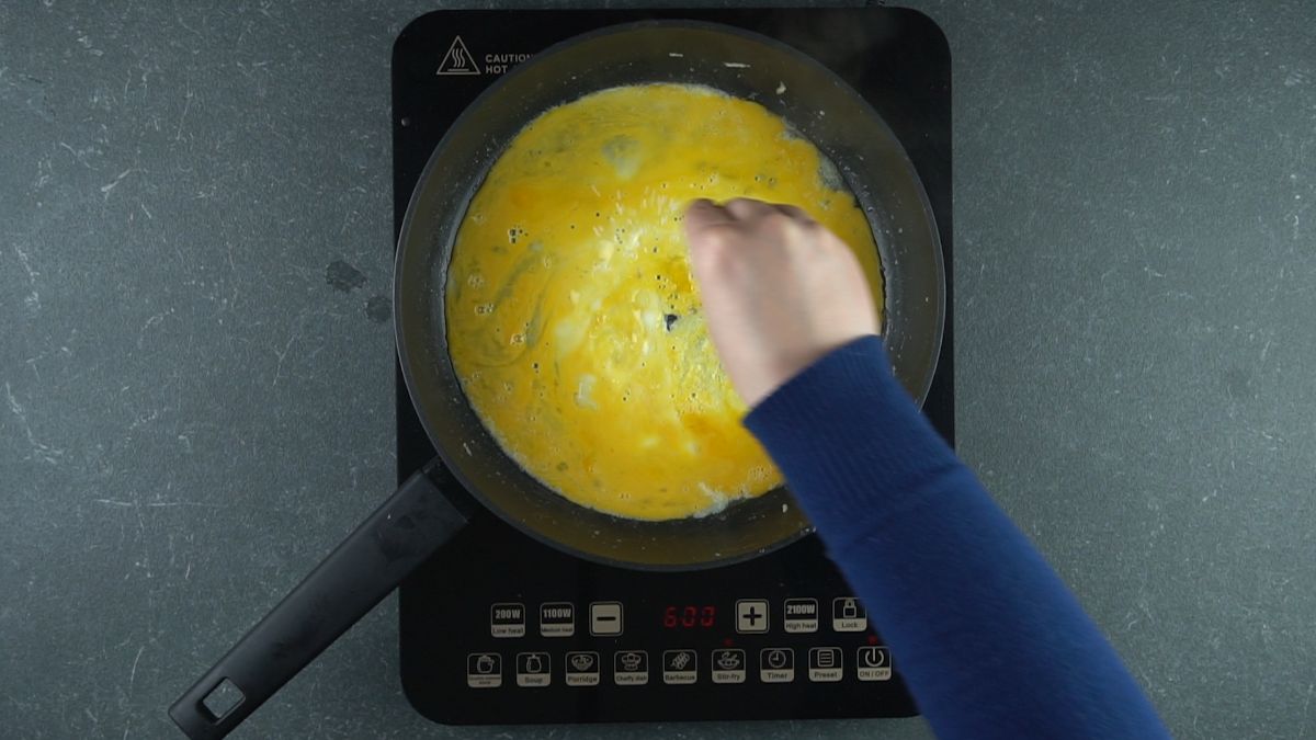 hand in blue shirt adding salt to eggs in skillet
