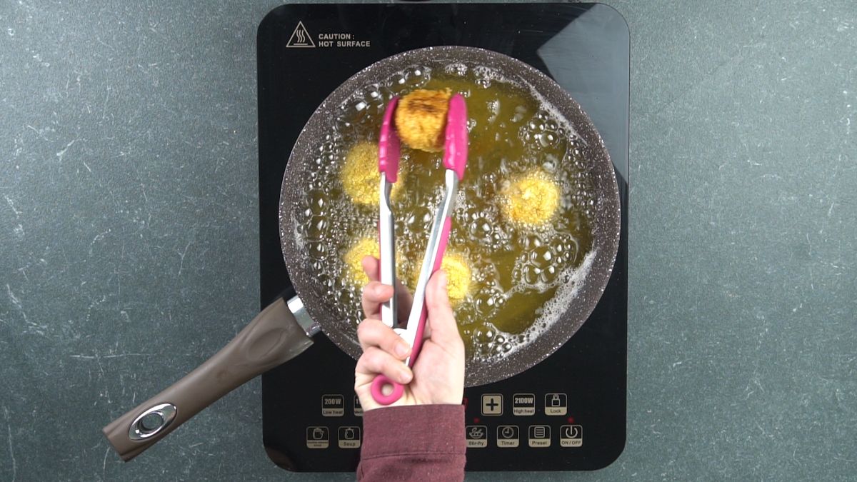 red tongs lifting fried chicken bombs out of oil in skillet