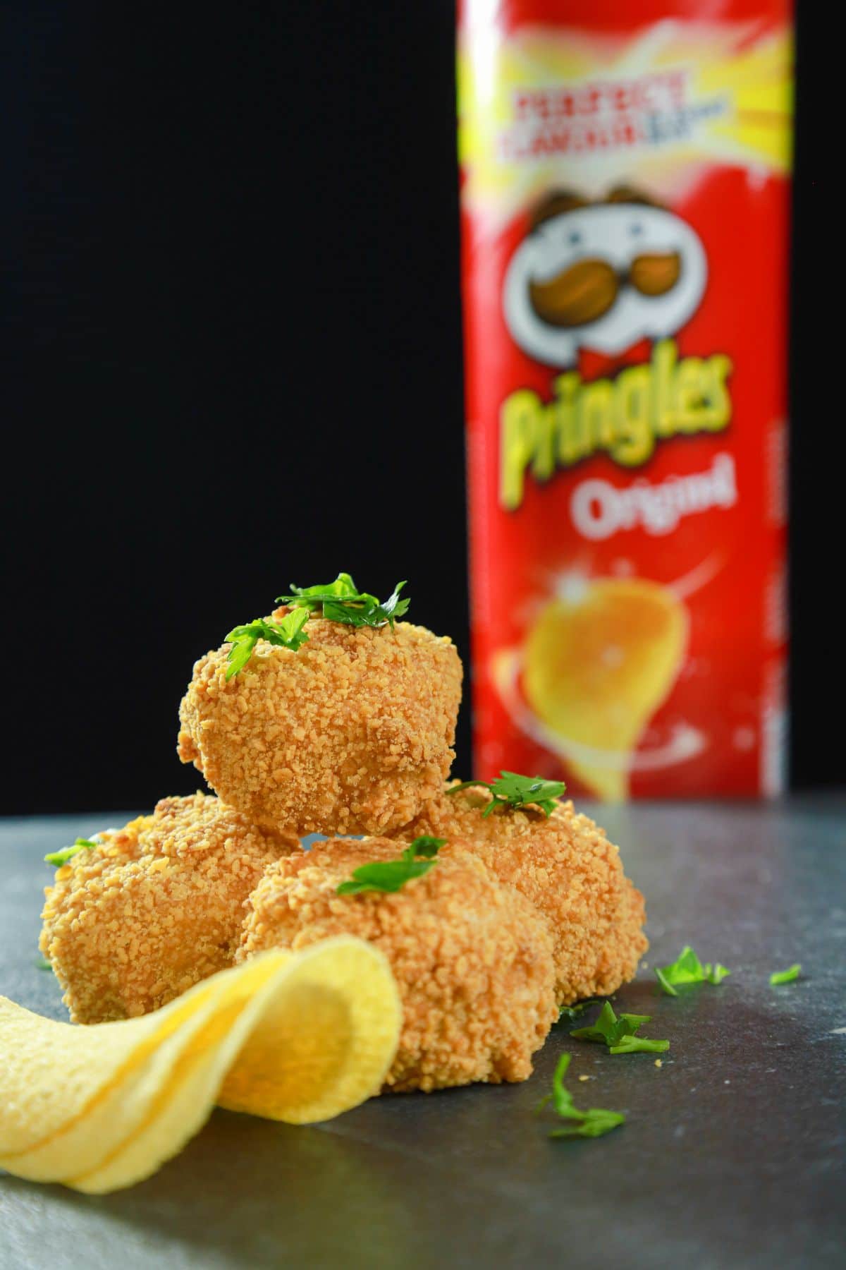 fried stuffed chicken bombs on grey table with chips and can of pringle sin background