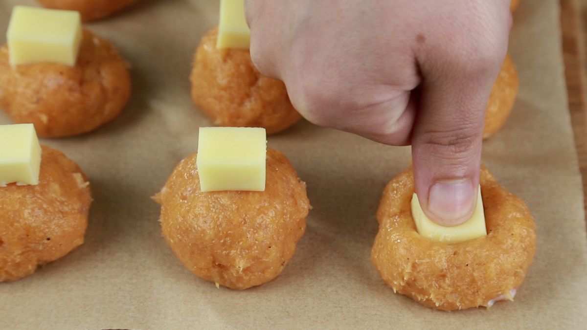 finger pushing cheese cube into ground chicken meatball