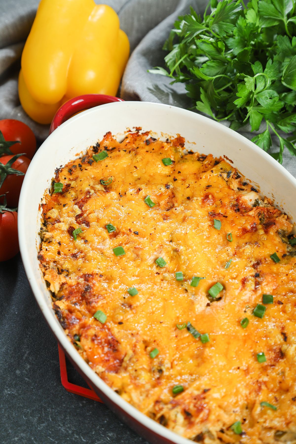 baked buffalo chicken dip in red and white oval baking dish with herbs and bell pepper in background