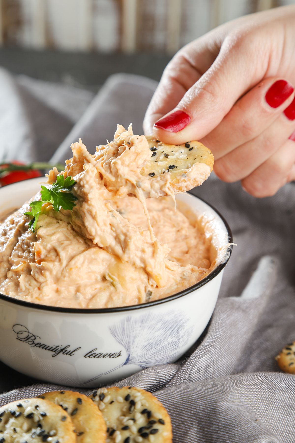 hand with red nails dipping into white bowl of dip with cracker