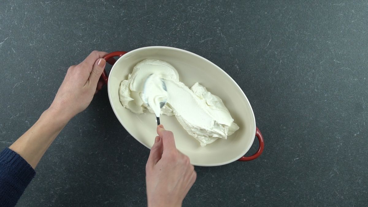 spoon spreading cream cheese over bottom of baking dish