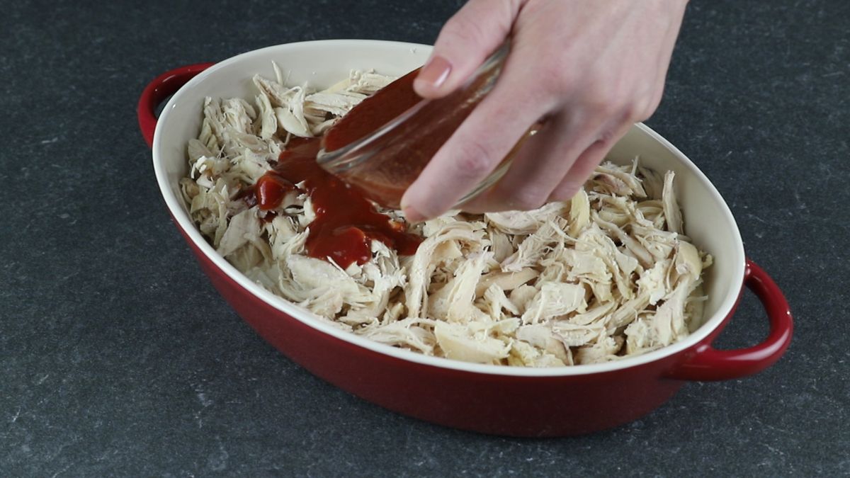 sauce being poured over chicken in red baking dish