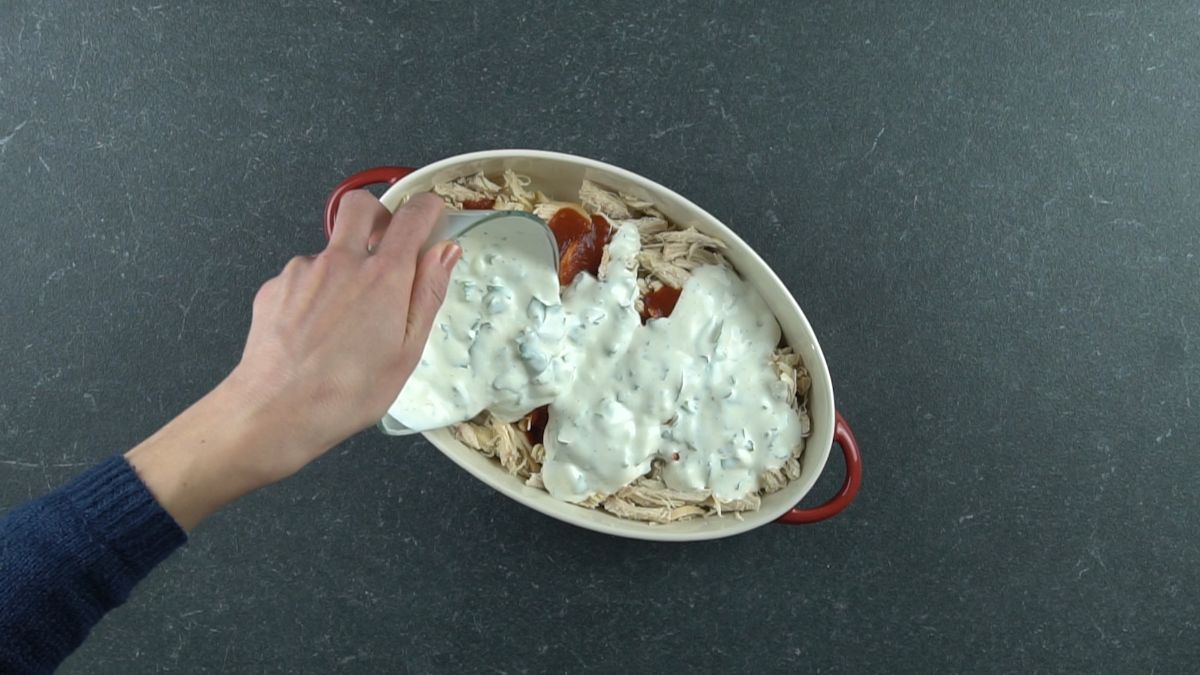 hand pouring ranch dressing over top of chicken in baking dish