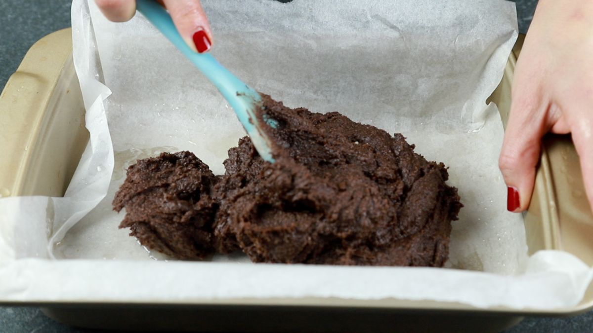 teal spoon spreading brownie batter over parchment paper