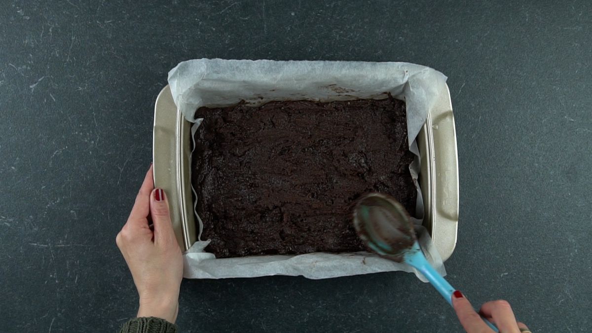 spoon spreading vegan brownie batter into pan