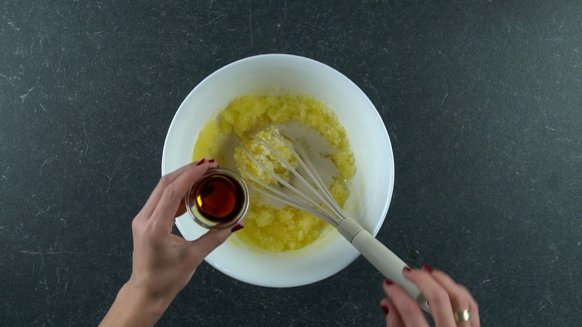 hand holding bowl of vanilla extract above bowl of yellow batter
