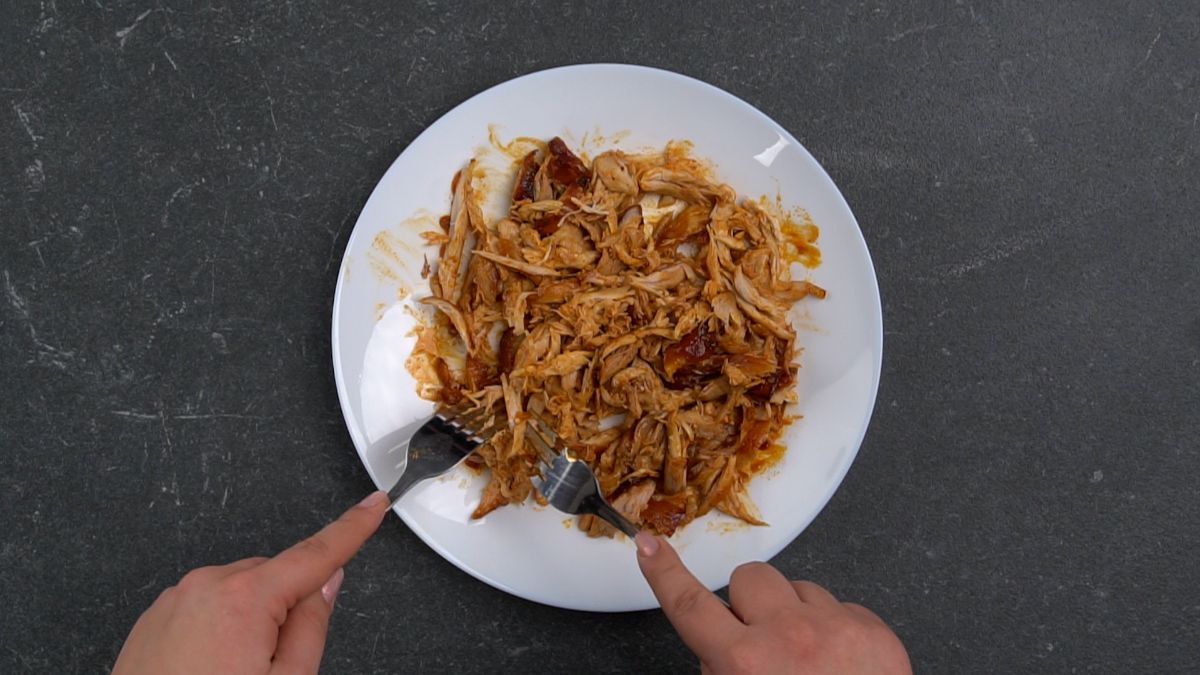 forks shredding chicken on white plate