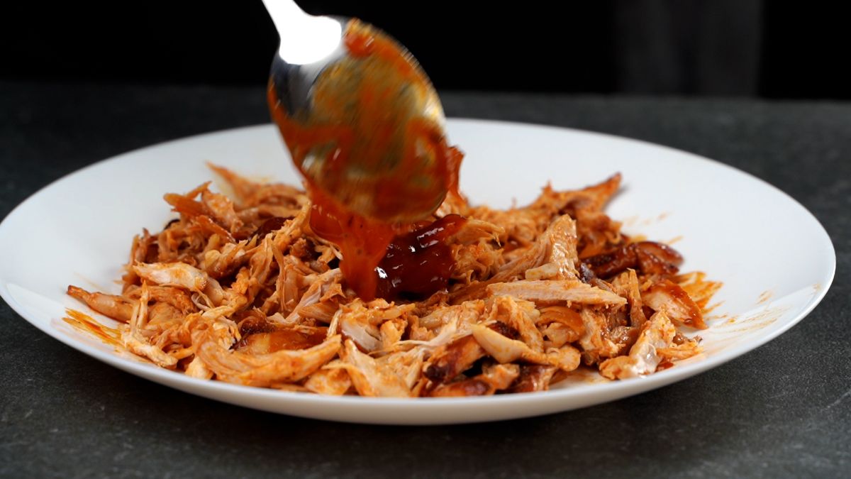 sauce being spooned onto plate of pulled chicken