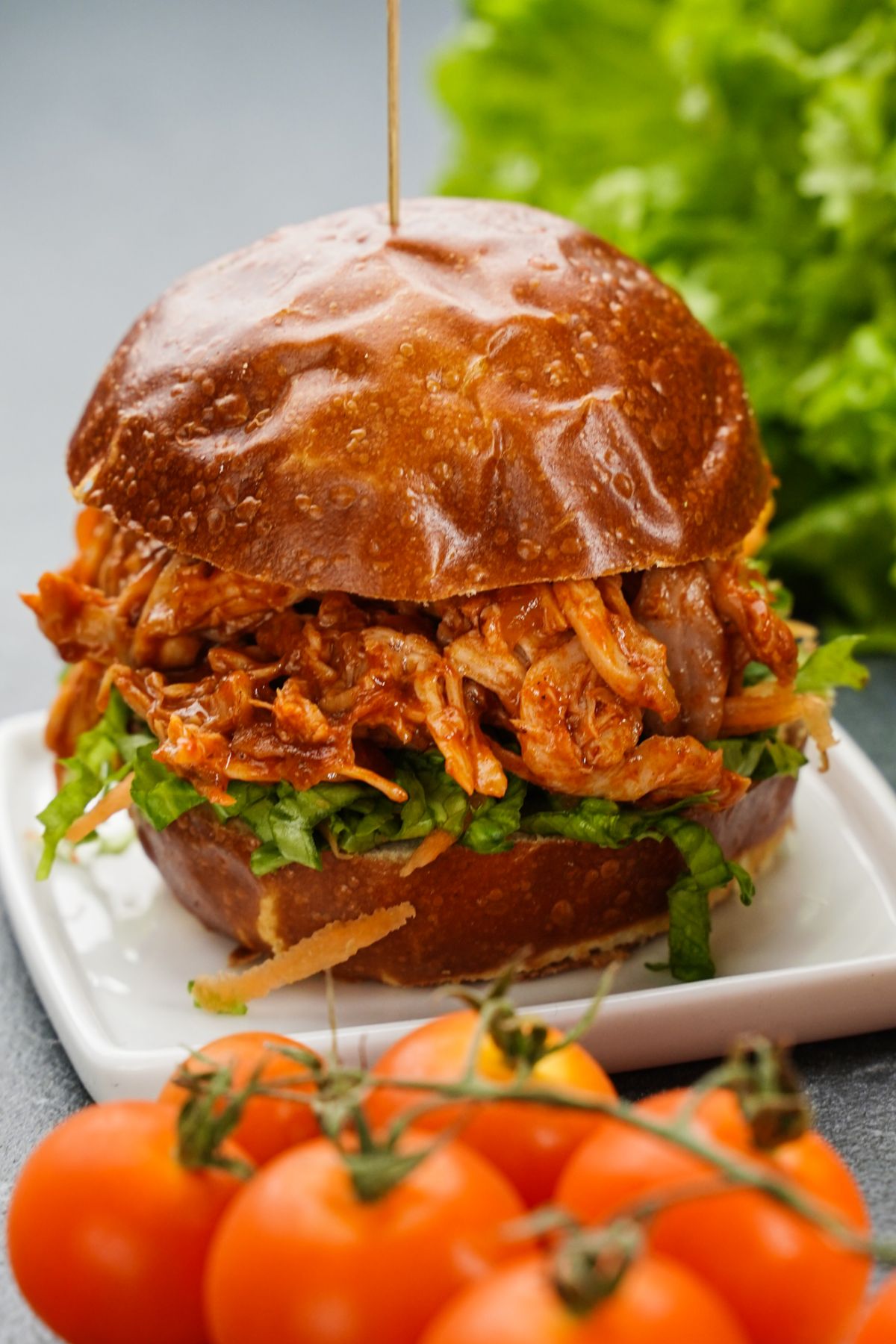 pulled chicken sandwich on white plate with lettuce in background