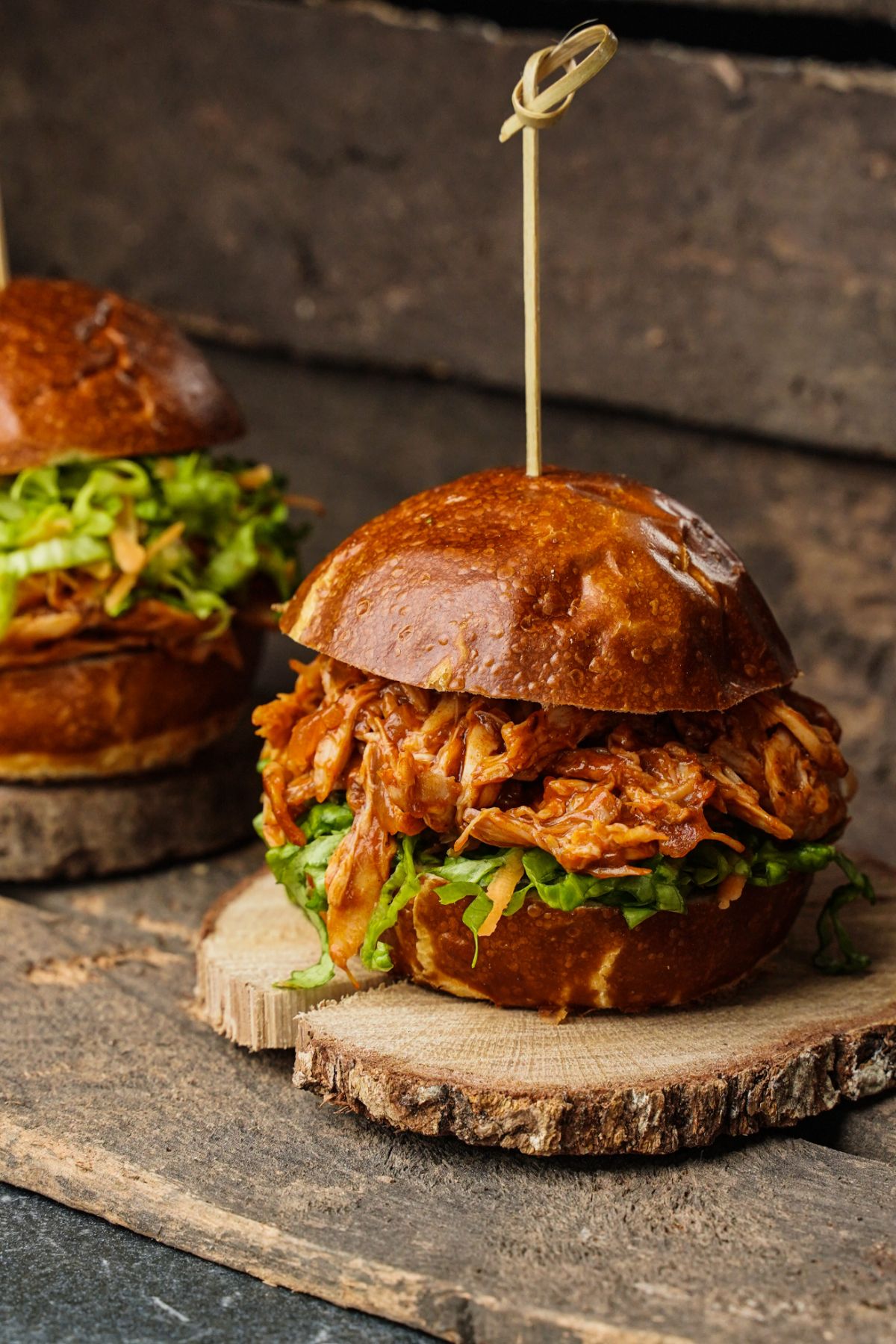 barbecue pulled chicken sandwiches on wood slices with toothpick in center of bun