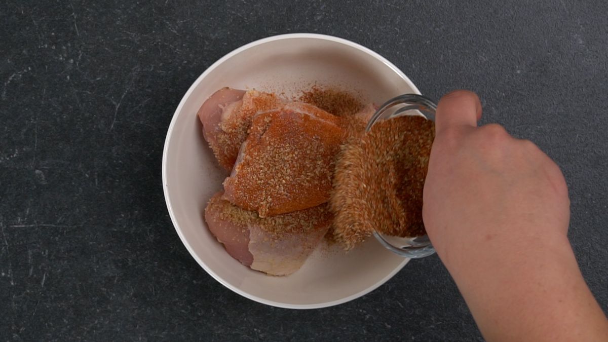 spice blend being poured over chicken legs in white bowl