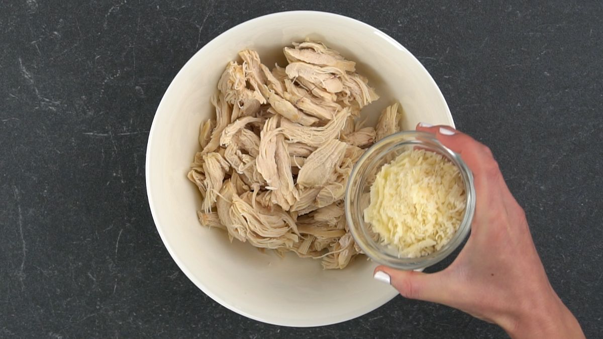 parmesan being poured over chicken in white bowl