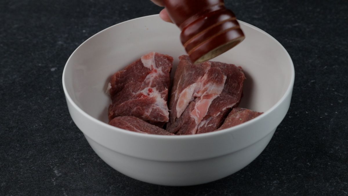 pepper being added to white bowl of beef chunks