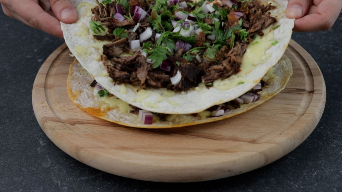 two tortillas stuffed with birria and cheese sitting on cutting board