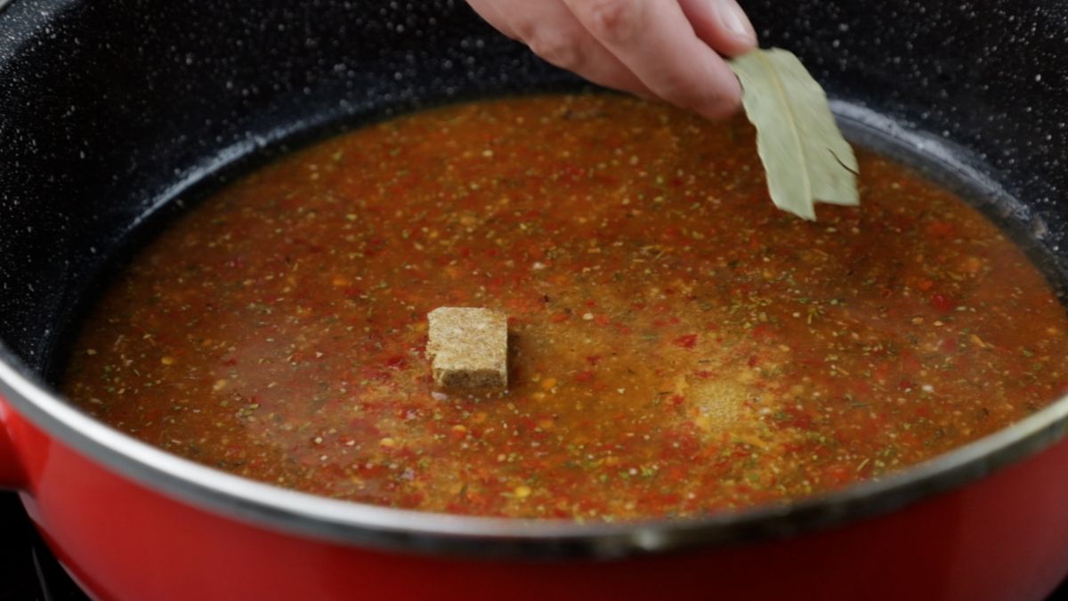 bouillon cube and bay leaf being added to sauce in skillet