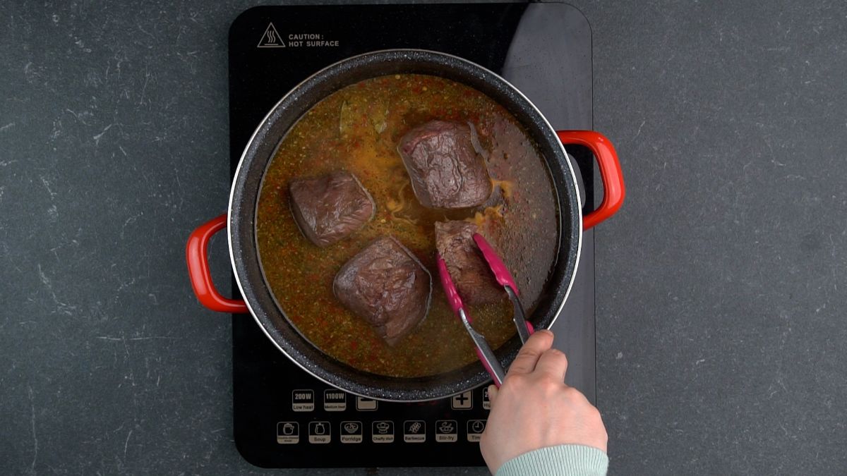 pink tongs placing beef pieces into red skillet