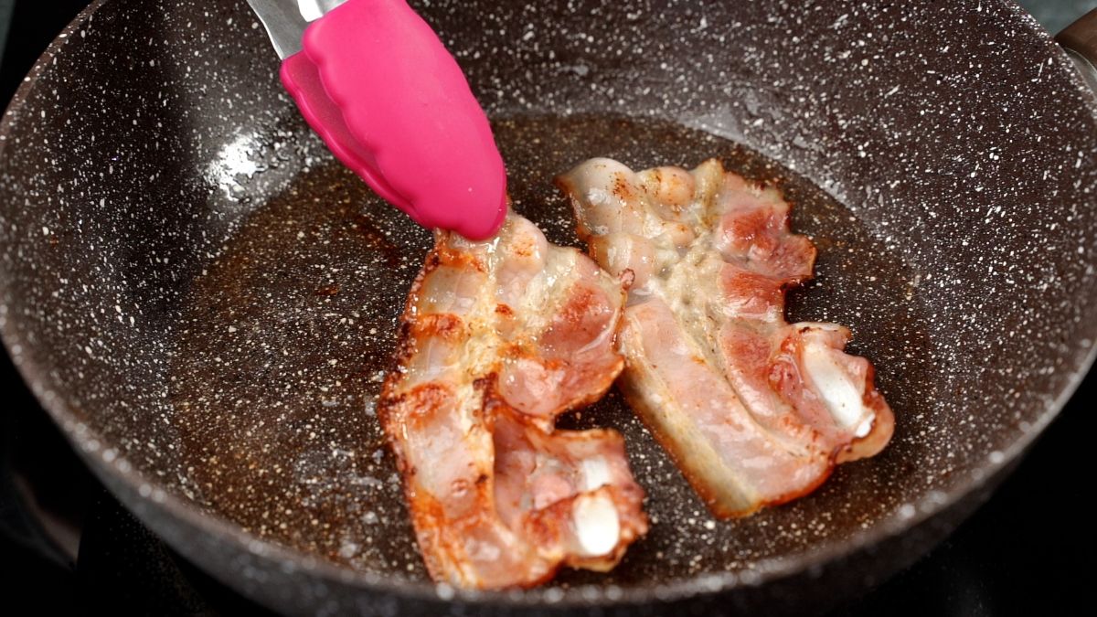 pink tongs turning bacon in skillet
