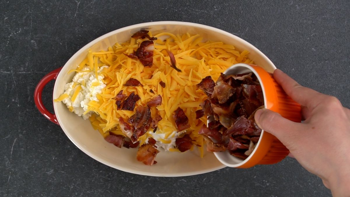 orange bowl of bacon being poured into oval baking dish with cheese